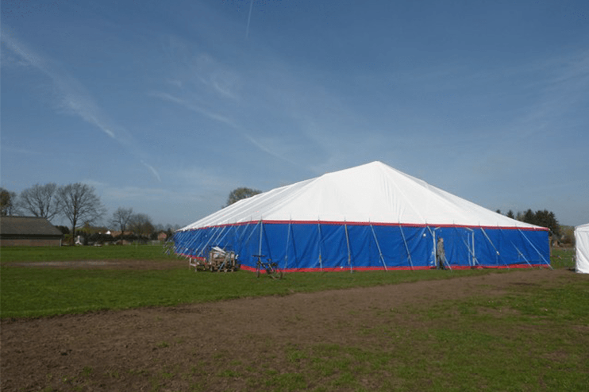 Large white, blue, and red tent in a green field under a clear sky.